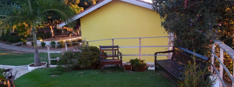 Chalé amarelo da pousada com bancos de madeira e jardim florido ao entardecer