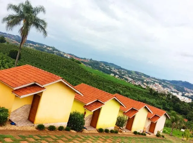 Chalés amarelos com telhado de cerâmica em morro verde, com a cidade e as montanhas ao fundo