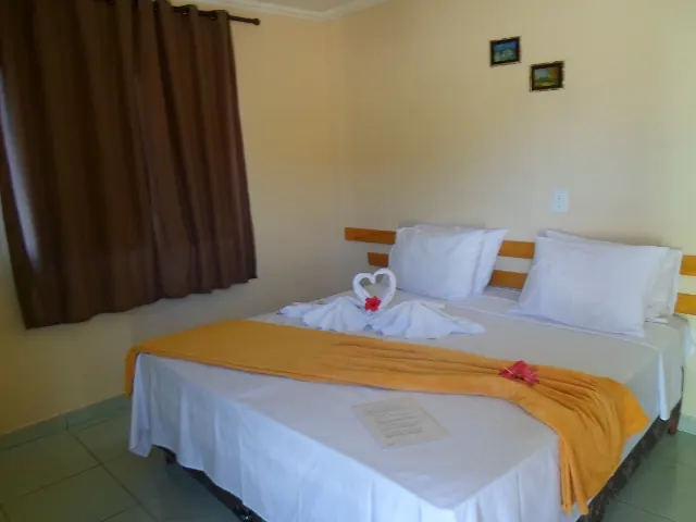 Quarto de casal com cabeceira de madeira, colcha laranja e toalhas dobradas em forma de coração