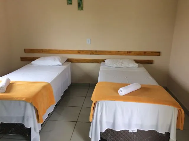 Quarto com duas camas de solteiro, colchas laranja e toalhas enroladas