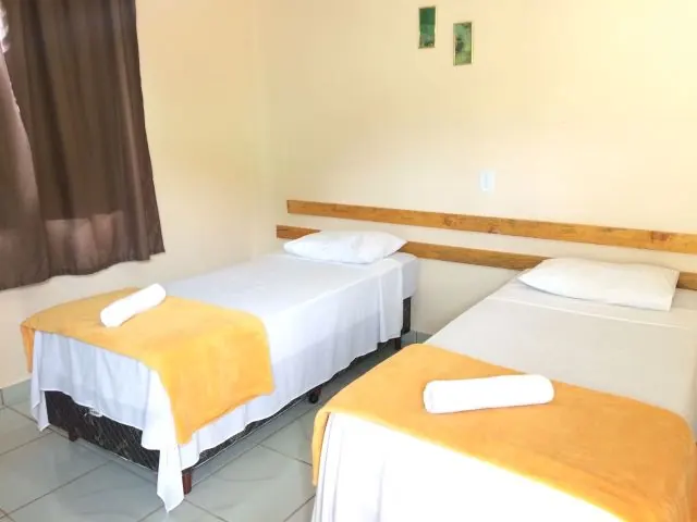 Quarto iluminado com duas camas de solteiro e arandelas de leitura na parede