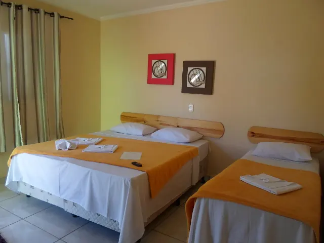 Quarto triplo com cama de casal, cama de solteiro e quadros coloridos na parede