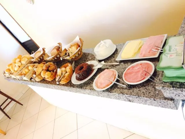 Balcão do café da manhã com pães, bolo de chocolate, presunto e queijo