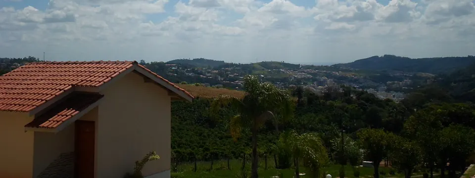 Chalé com telhado de cerâmica e vista para a cidade de Serra Negra entre morros e mata